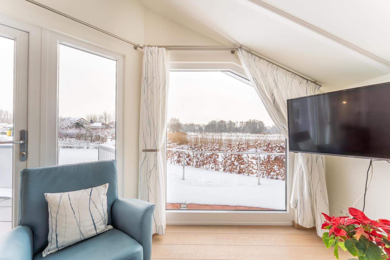 A room with a blue armchair, TV, and view of a snowy landscape.