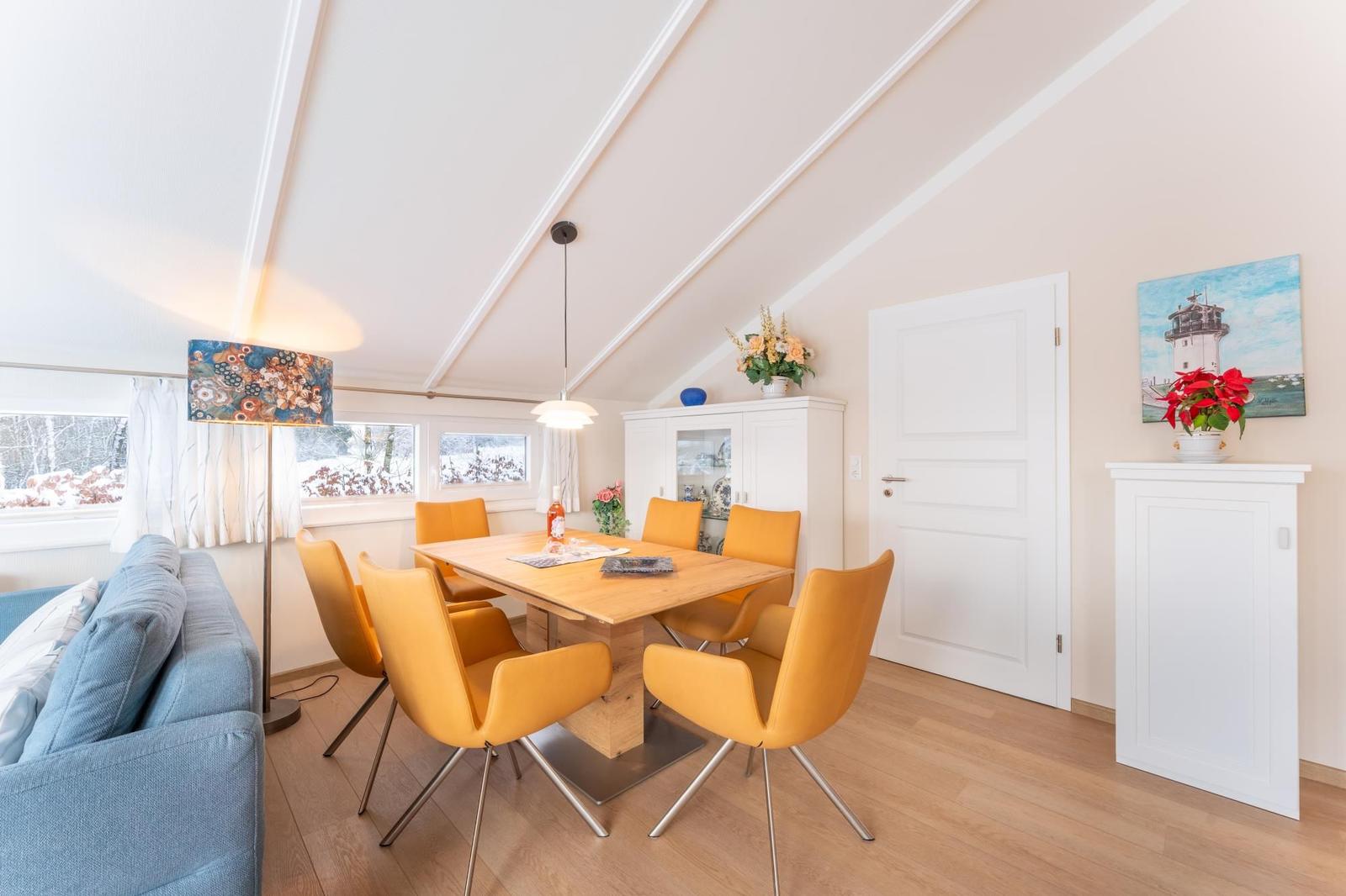 Dining room with wooden table, yellow chairs, and windows overlooking snow.