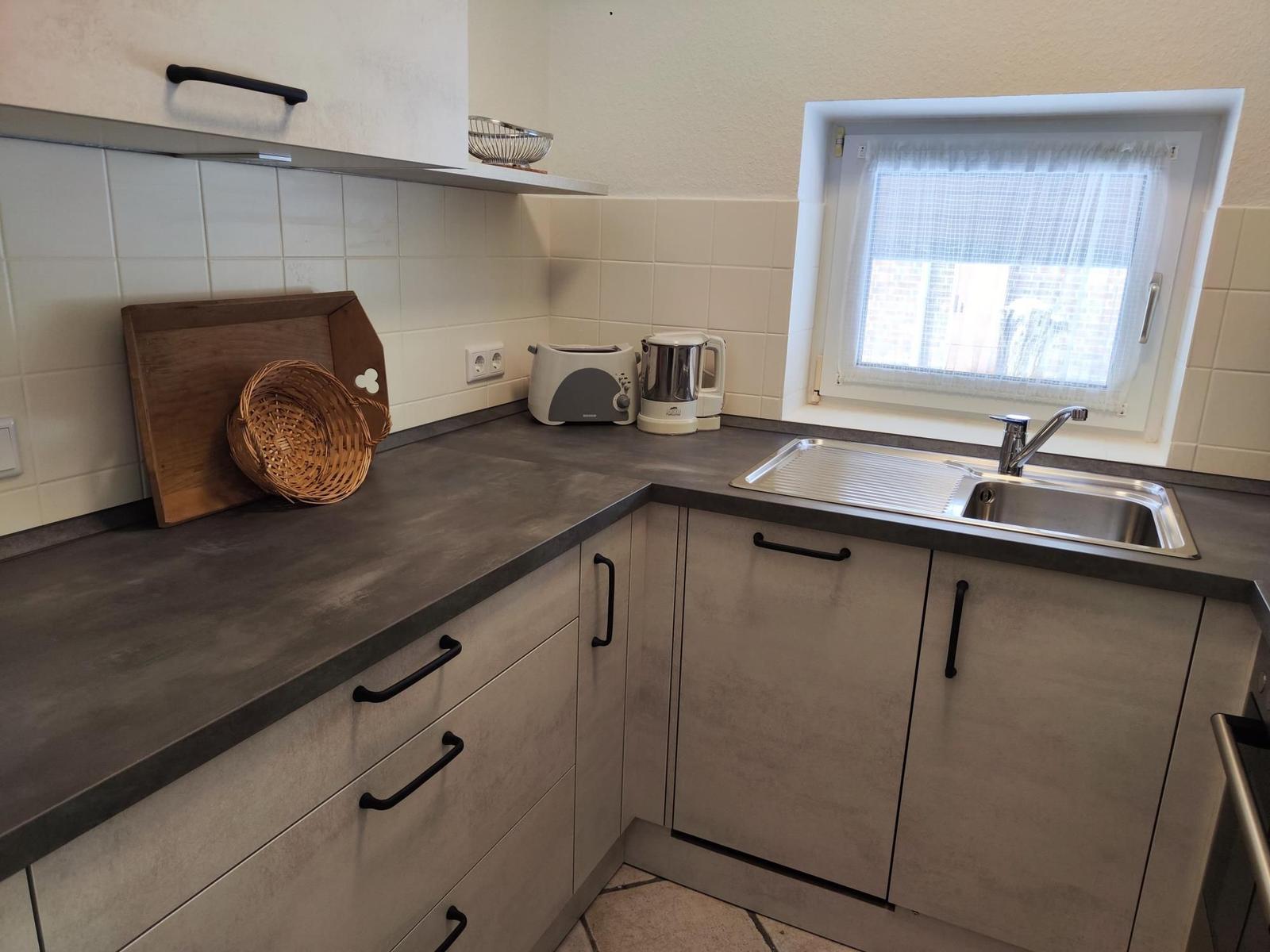 Küche mit Arbeitsplatte, Spüle und Fenster. Auf der Arbeitsfläche stehen ein Toaster und eine Kaffeemaschine.