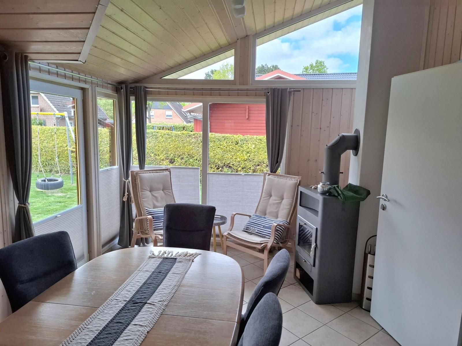 Sitzbereich mit Tisch und Stühlen, Holzdecke und Fenster zur Außenterrasse.