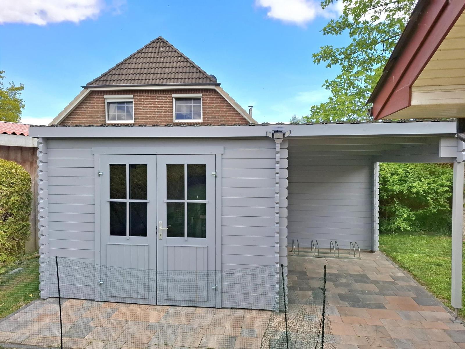 Graue Garage mit Doppeltür und überdachtem Bereich für Fahrräder.