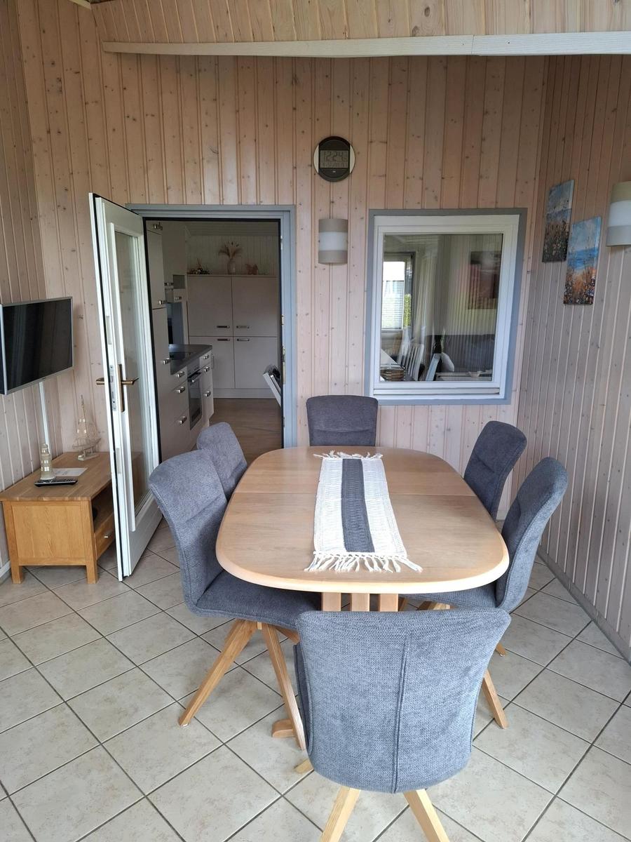 Esszimmer mit Holztisch, sechs Stühlen und Blick in die Küche.