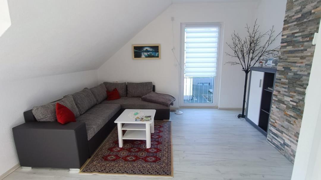 Wohnzimmer mit Ecksofa, Tisch und Fenster zur Terrasse.