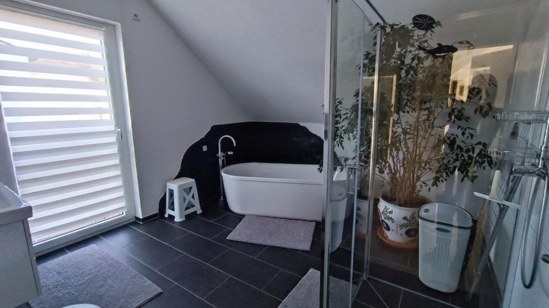 Badezimmer mit freistehender Badewanne, Dusche und Fenster mit Jalousie.