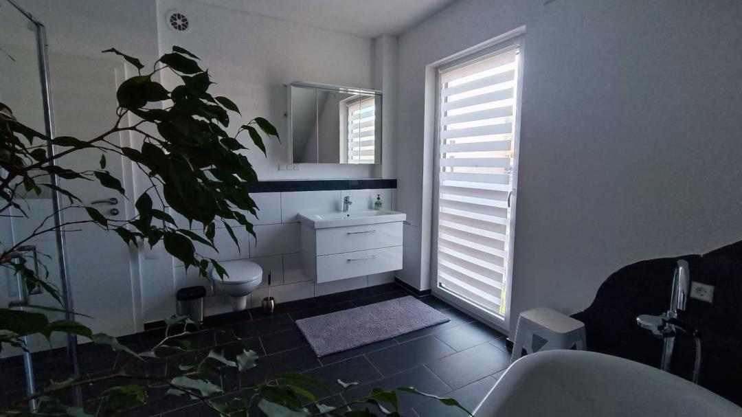 Badezimmer mit Dusche, Waschbecken und Badewanne. Fenster mit Jalousie.