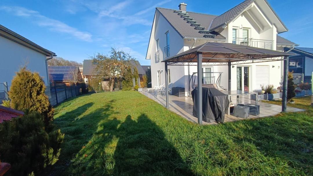 Haus mit Garten und Terrasse unter Markise. Grünfläche und Pflanzen sichtbar.