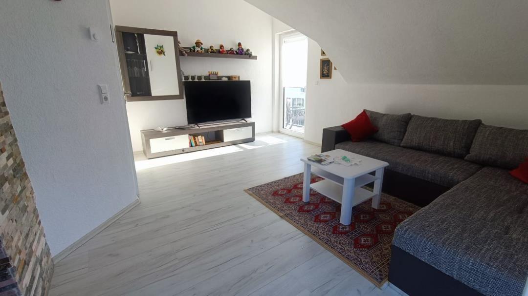 Wohnzimmer mit Sofa, TV und Balkonzugang.