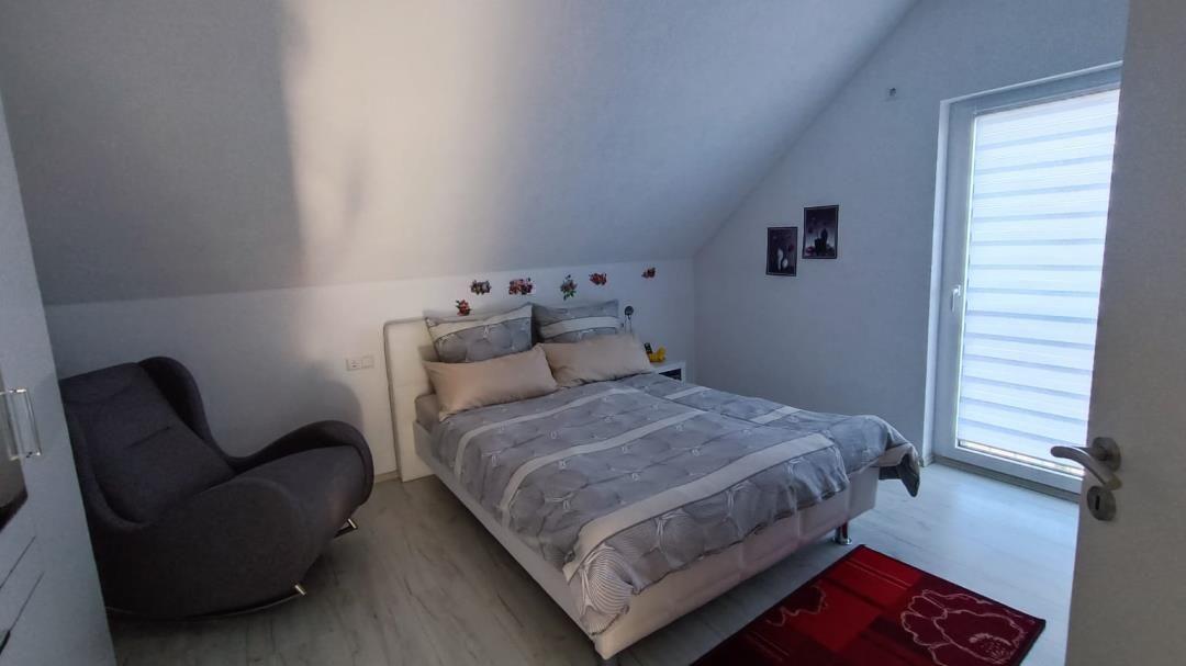Schlafzimmer mit Dachschrägen, Bett, Sessel und Fenster mit Jalousie.