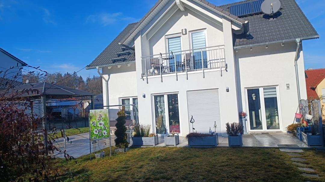 Moderne weiße Villa mit Balkon, Garten und Solaranlage. Terrasse mit Pflanzen und Gartentor.