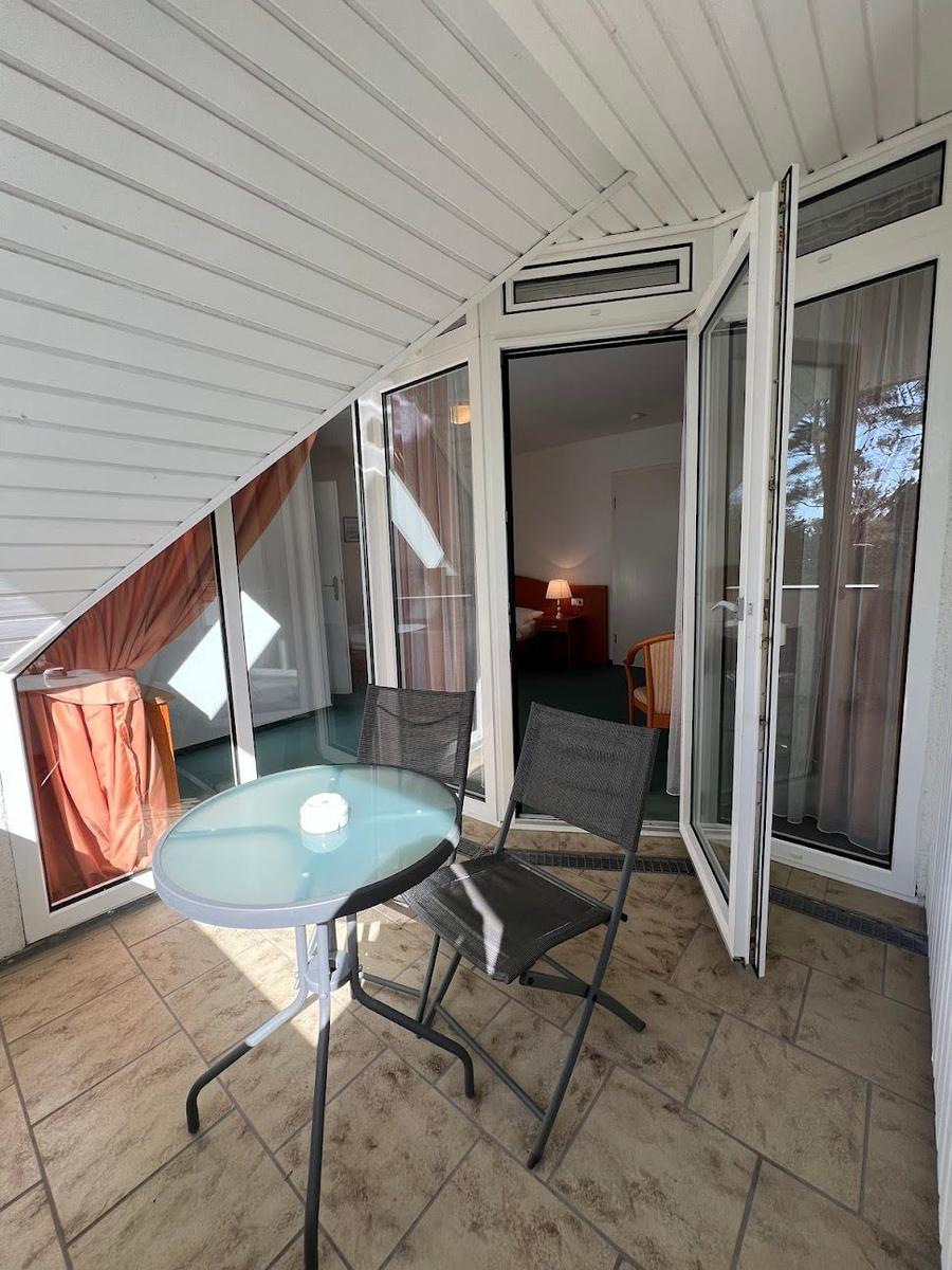 Terrasse mit Tisch und zwei Stühlen, Tür führt ins Zimmer.
