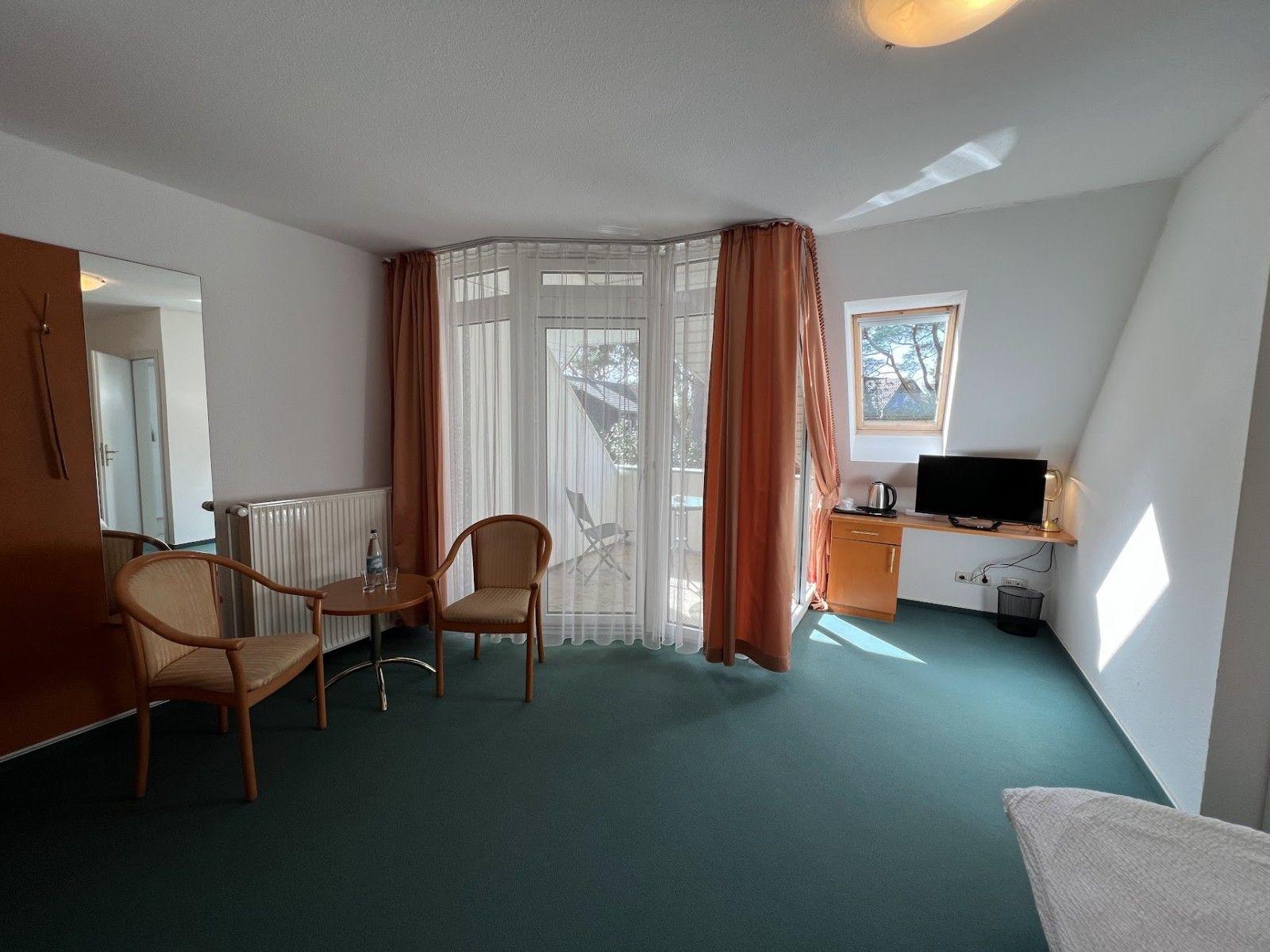 Zimmer mit Sitzbereich, Balkon und Schreibtisch mit TV.