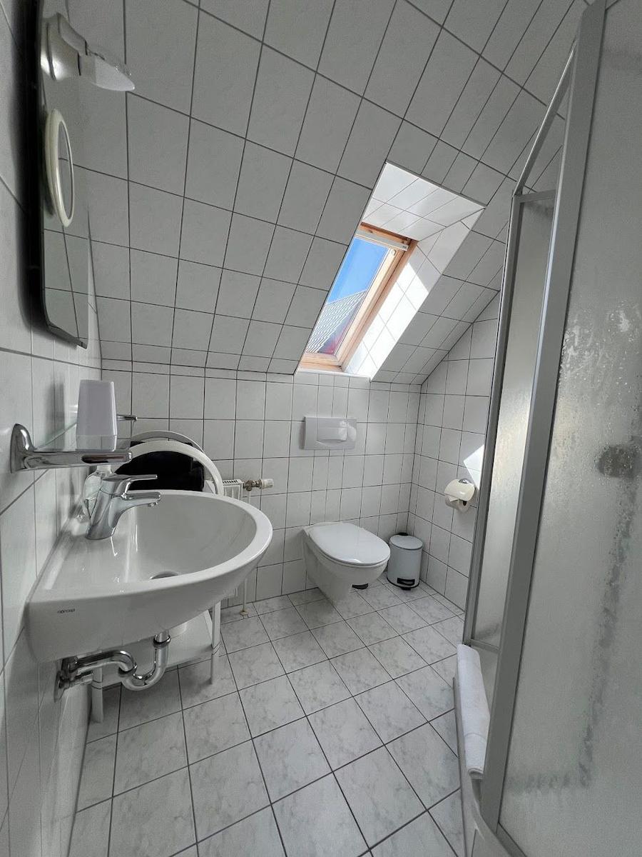 Badezimmer mit Dusche, WC und Waschbecken unter Dachschräge mit Fenster.