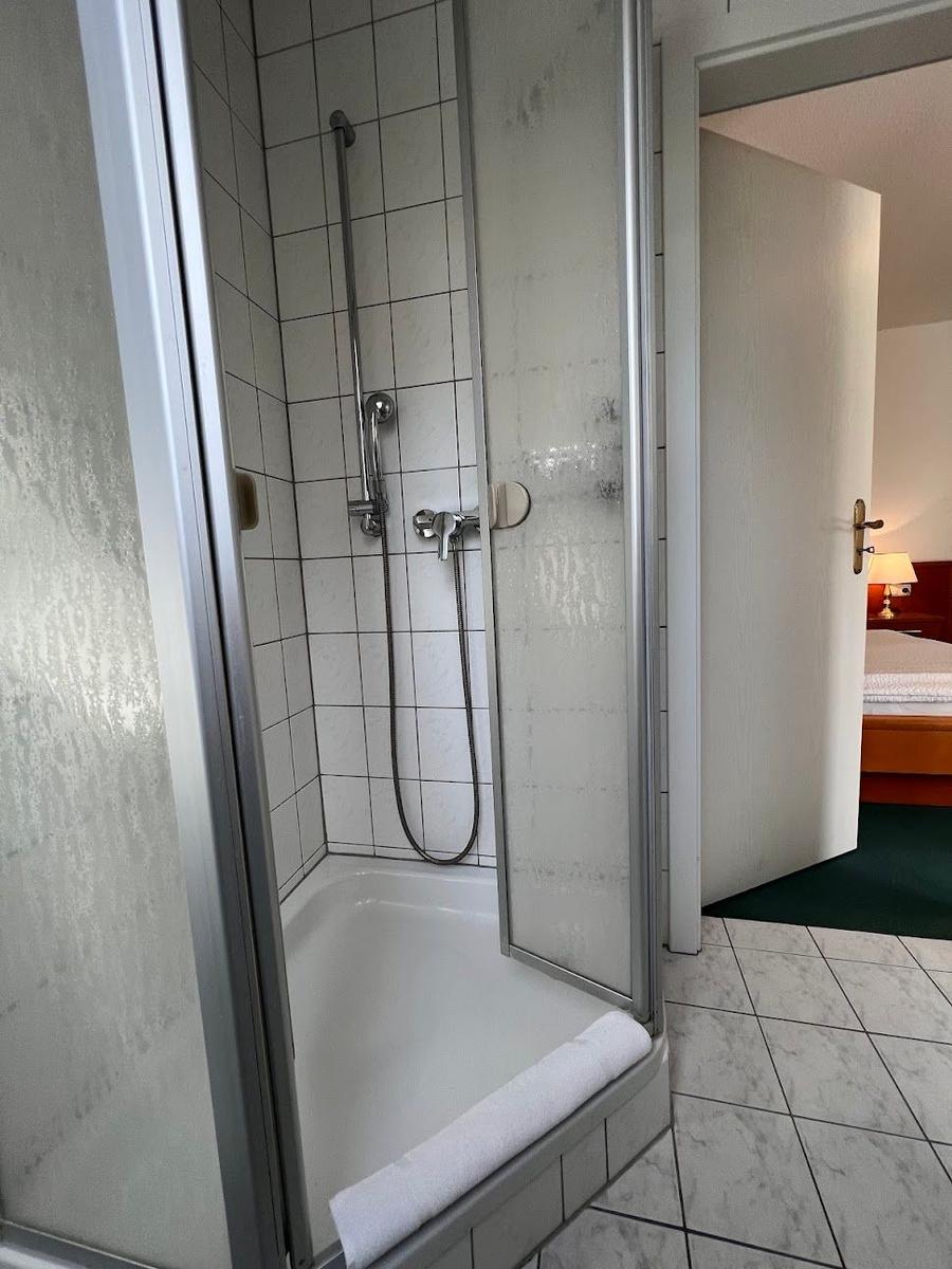 Dusche mit Duschbrause und Handbrause, Tür zum Schlafzimmer sichtbar.