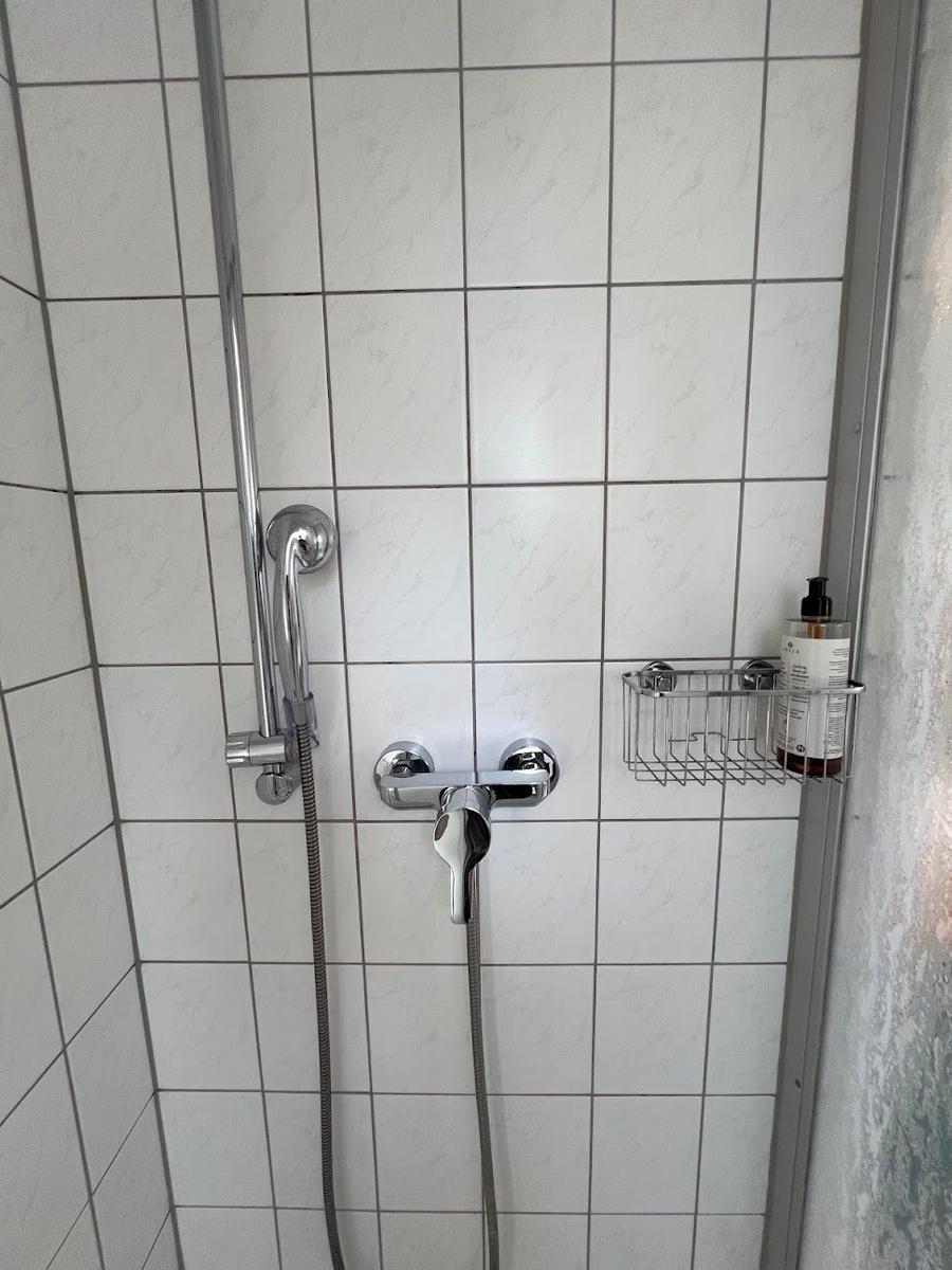 Dusche mit Duschbrause, Wasserhahn und Seifenspender im Badezimmer.