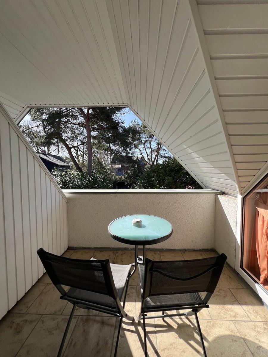 Terrasse mit Tisch und zwei Stühlen, Blick auf Bäume und Himmel.
