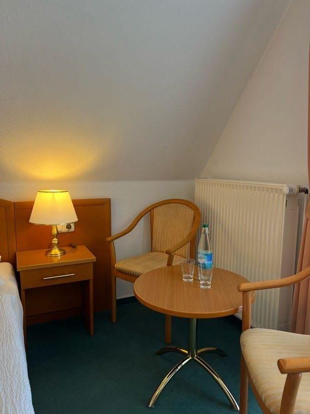 Zimmer mit Holztisch, zwei Stühlen, Nachttisch und Lampe unter schräger Decke.