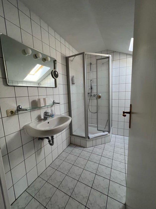 Badezimmer mit Dusche, Waschbecken und Spiegel an der Wand.