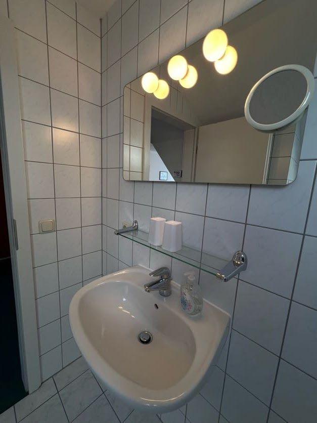 Badezimmer mit Waschbecken, Spiegel und beleuchteter Wand