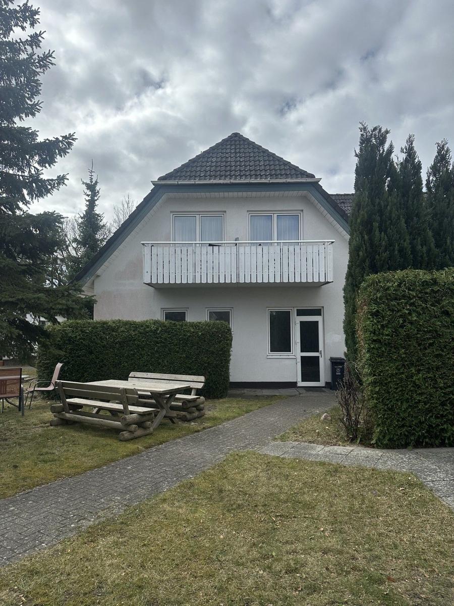 Zwei-Stöckiges Haus mit Balkon, Terrasse und Gartenbereich. Umgeben von Bäumen und Hecken.