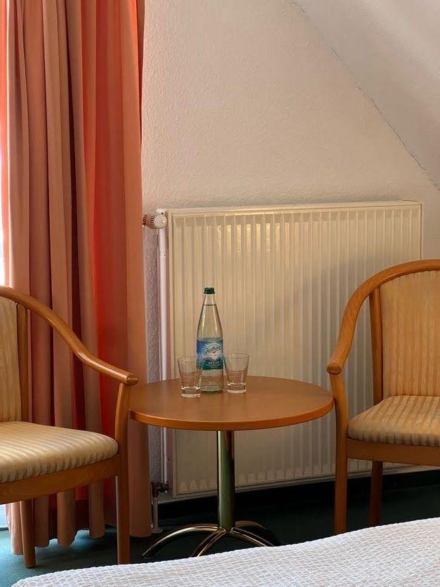 Zwei Stühle und ein Tisch mit Wasserflasche und Gläsern vor Heizkörper und Vorhang.