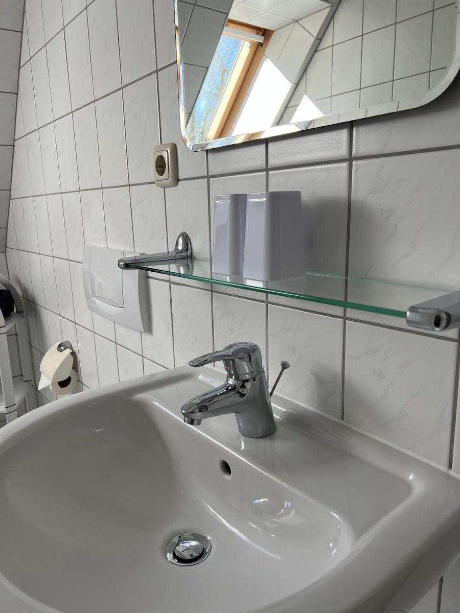 Bad mit Waschbecken, Spiegel und Glasregal an der Wand