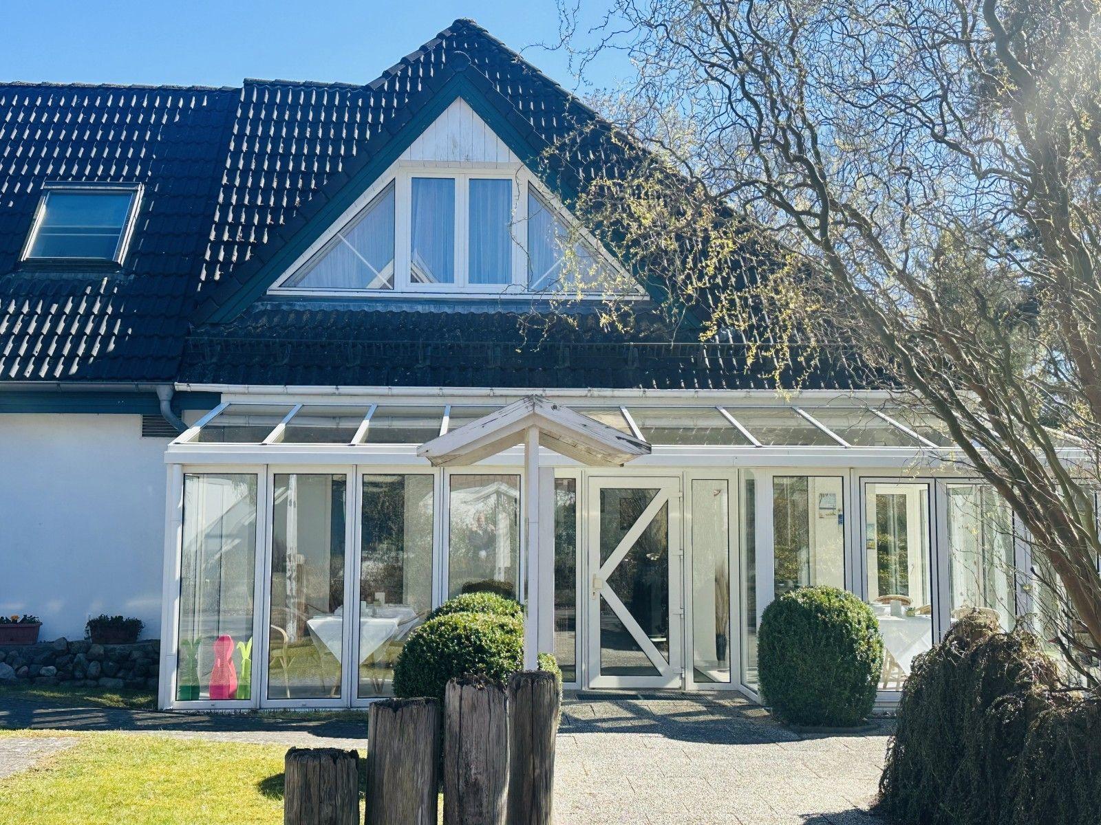 Haus mit Glasveranda und Dachfenster, umgeben von Bäumen und Gras.
