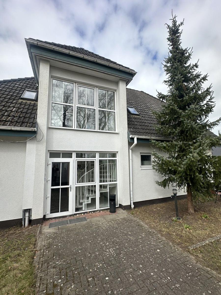 Haus mit großem Fenster und Eingangstür. Links ein großer Baum.