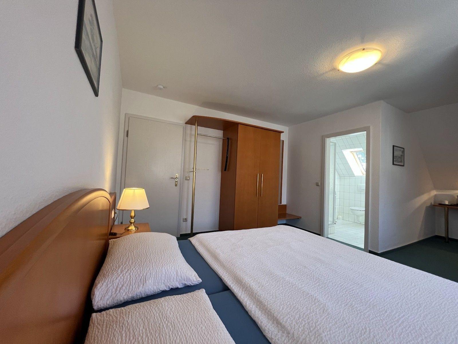 Schlafzimmer mit Bett, Kleiderschrank und angrenzender Badewanne.
