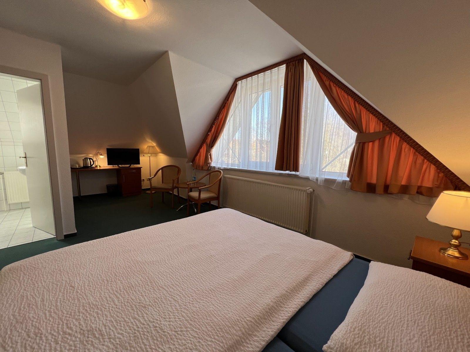 Ein Schlafzimmer mit Dachschrägen, Bett, Schreibtisch und Fenster mit Vorhängen.