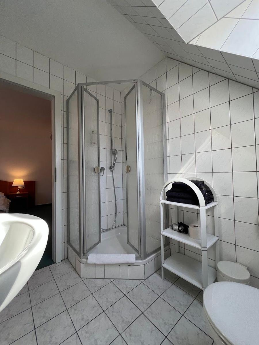 Badezimmer mit Dusche, Waschbecken und Toilette. Weiße Fliesen und Duschabtrennung.