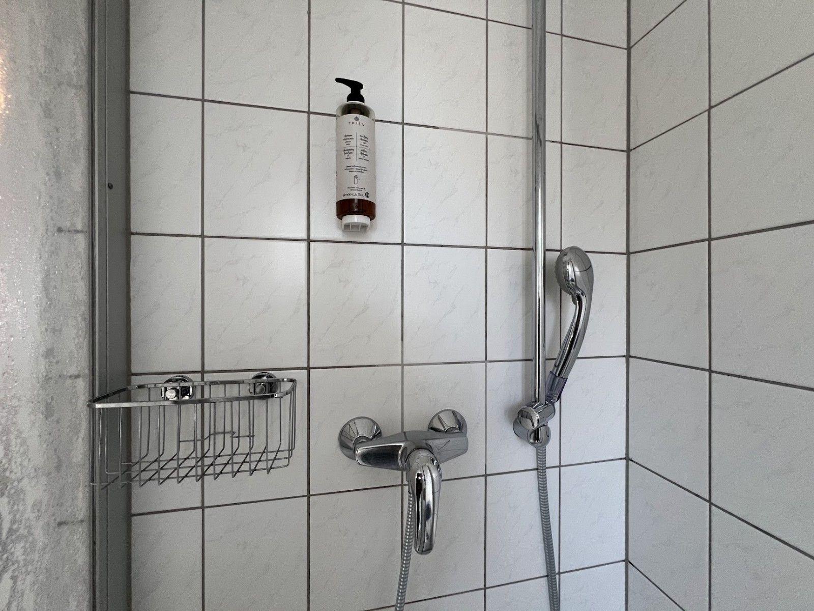 Duschkabine mit Duschbrause, Handtuchhalter und Flasche Duschgel.