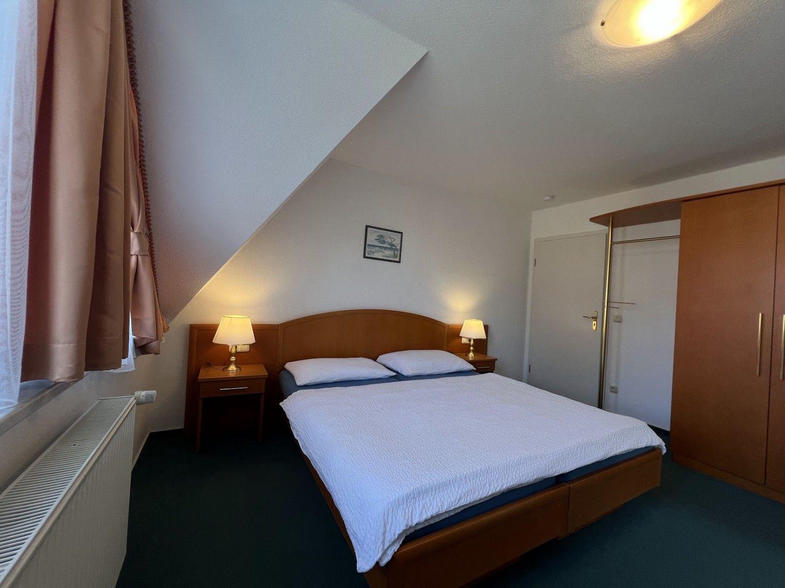 Schlafzimmer mit Doppelbett, Nachttischen und Kleiderschrank unter schrägem Dach.