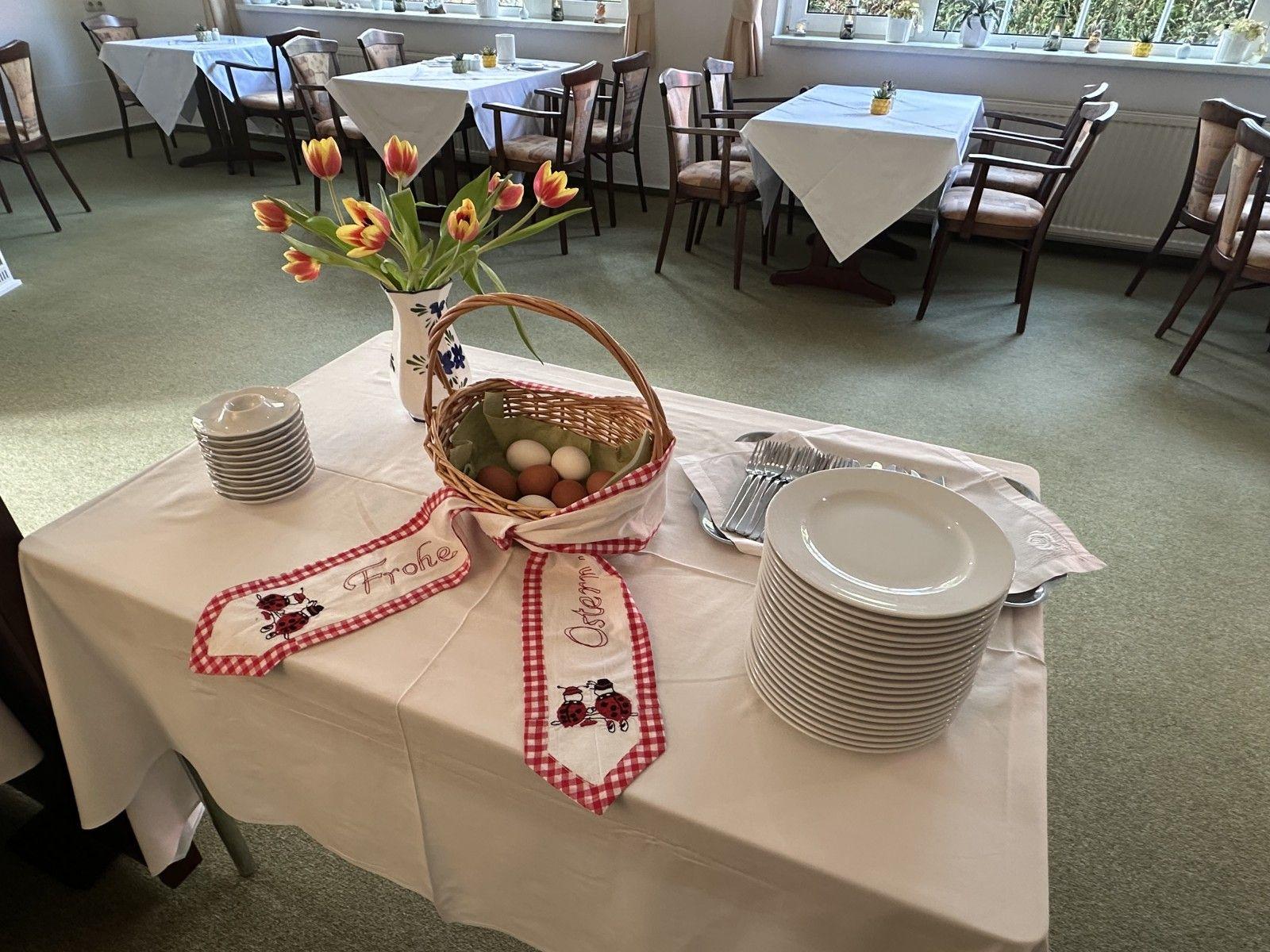 Tisch mit Tischdecke, Teller, Gabeln, Blumen und Eierkorb für Osterfest.