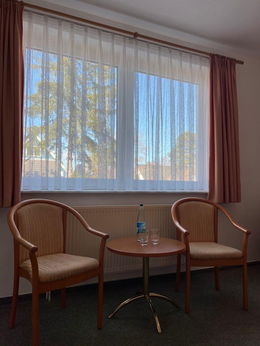 Zwei Stühle und ein Tisch stehen vor einem Fenster mit Vorhängen.