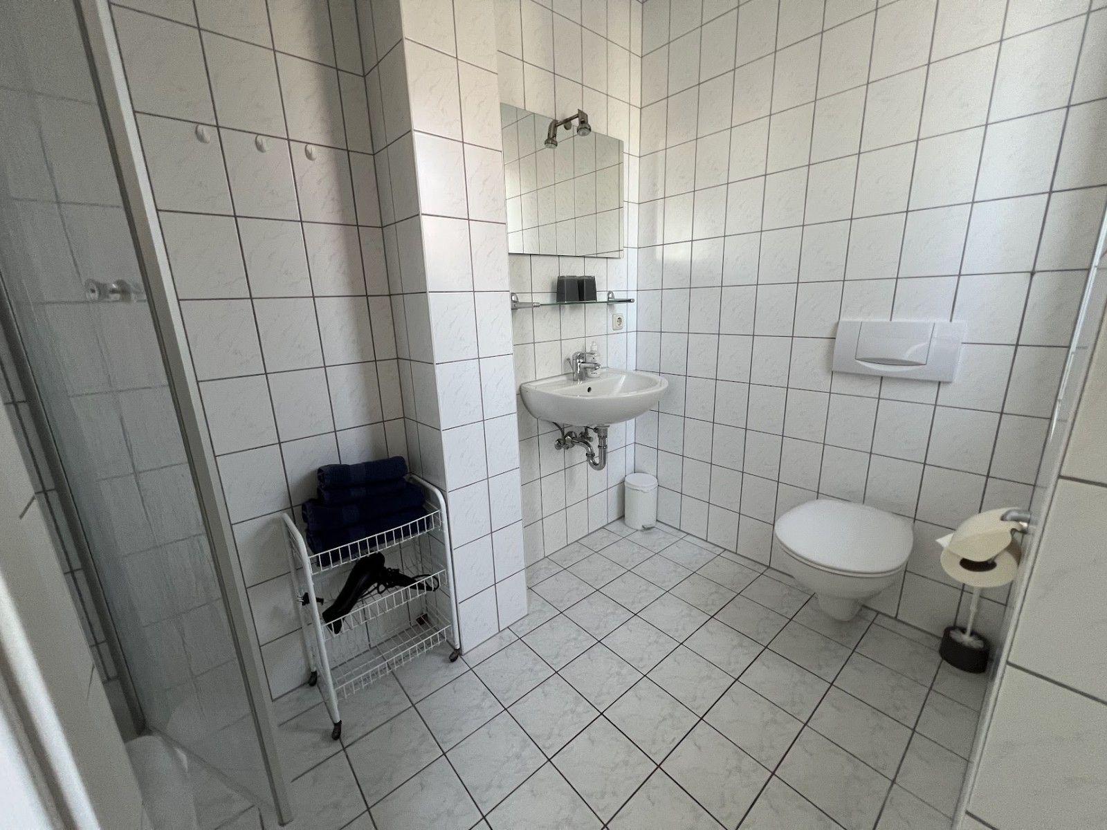 Badezimmer mit Dusche, Waschbecken, Toilette und Handtuchwagen.
