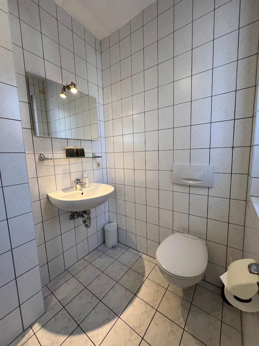 Badezimmer mit Waschbecken, Spiegel, Toilette und WC-Behälter.