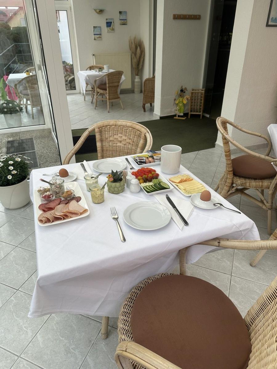 Tisch mit Frühstück auf Terrasse. Wickerstühle, weiße Tischdecke, Essen und Getränke.