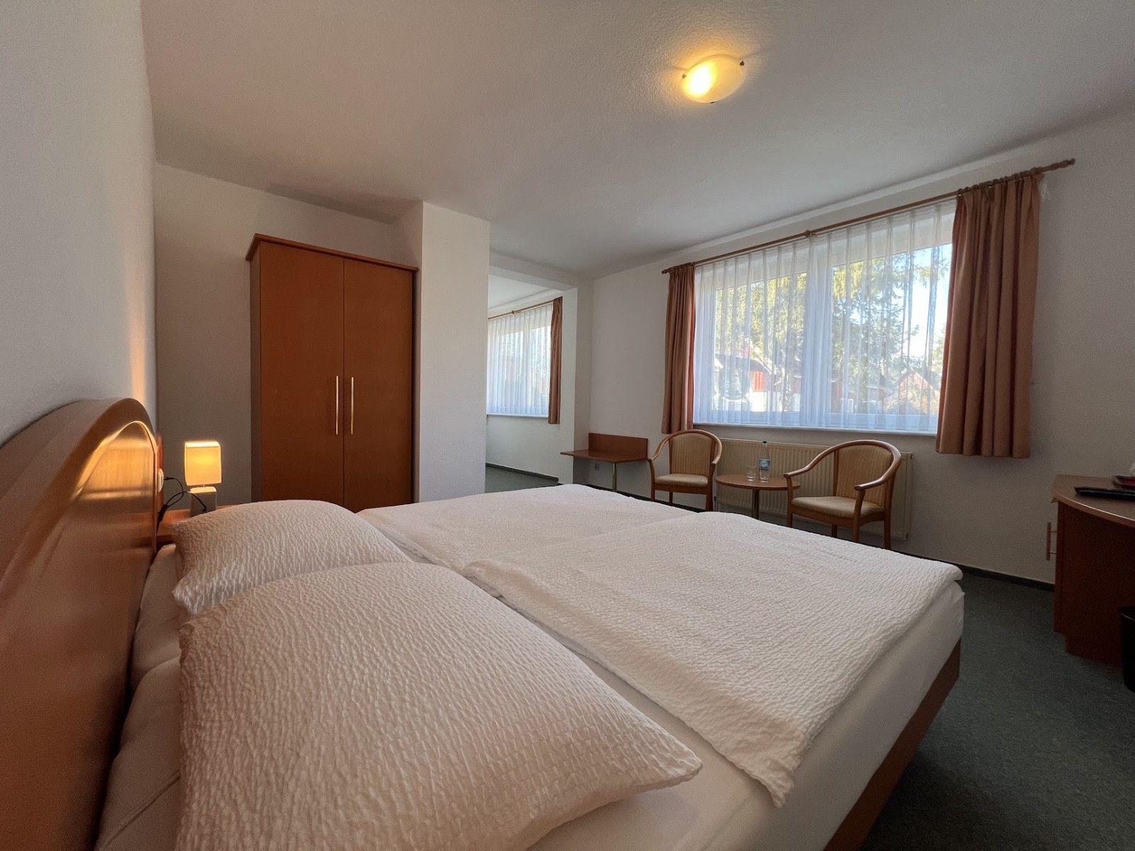 Schlafzimmer mit Doppelbett, Kleiderschrank, Sitzgelegenheit und Fenster mit Vorhängen.