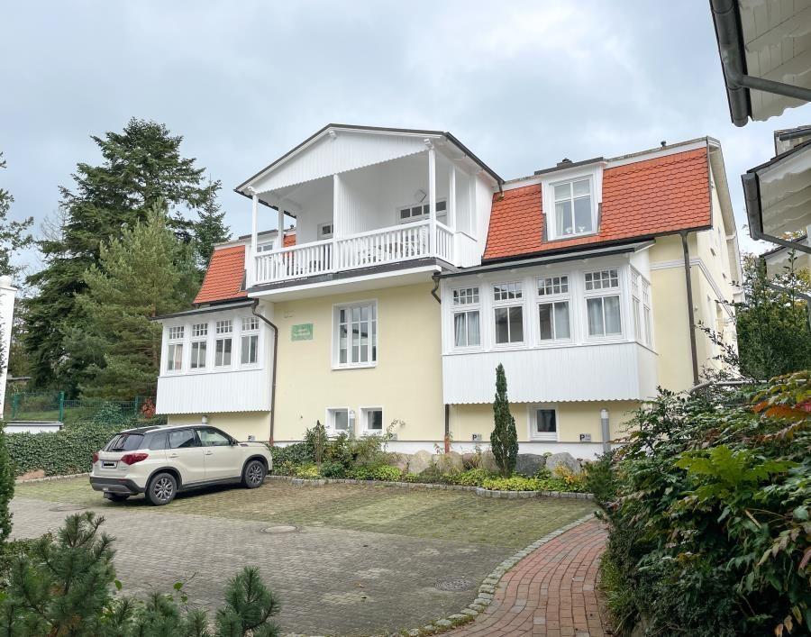 Haus mit Balkon, rotem Dach und gepflasterter Hof. Ein Auto steht auf dem Hof.