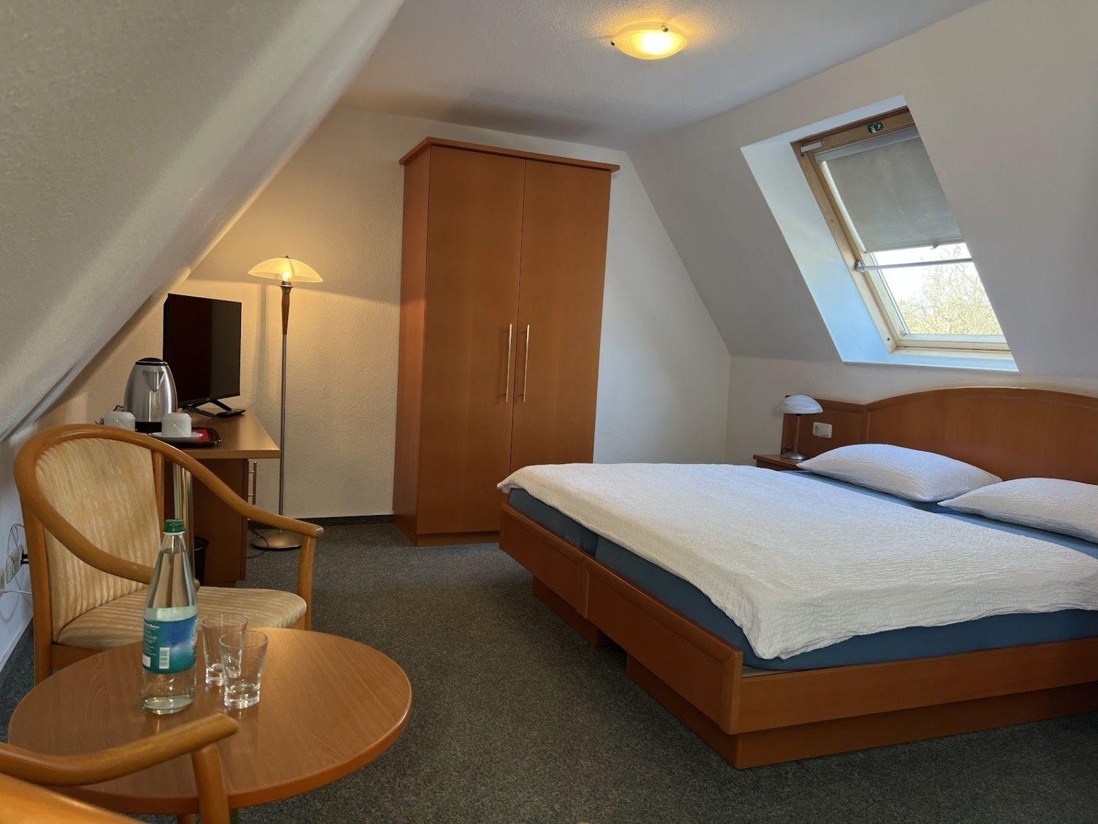 Zimmer mit Doppelbett, Schrank, Sitzgelegenheit und Dachfenster.