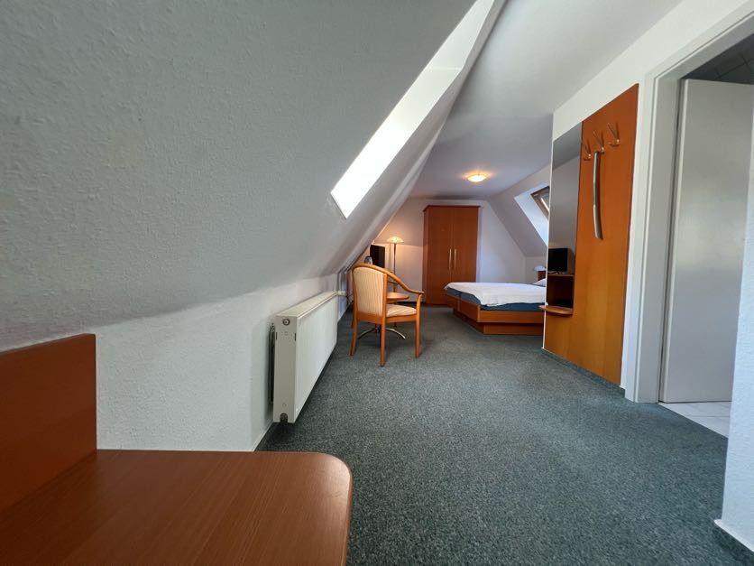 Dachgeschosszimmer mit Schlafplatz, Schreibtisch und Dachschräge. Holzmöbel und Heizung sichtbar.