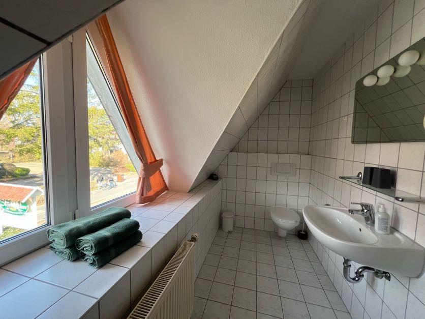 Badezimmer mit Fenster, Toilette, Waschbecken und Handtüchern.