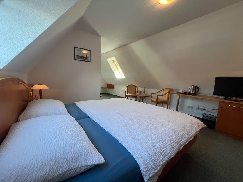 Doppelbett, Schreibtisch, zwei Stühle und Fernseher in einem Schlafzimmer mit Dachschrägen.