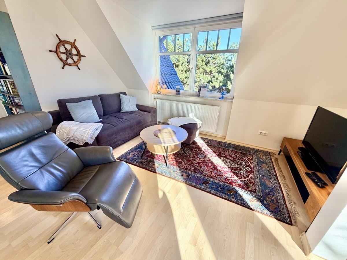 Wohnzimmer mit Sofa, Sessel, TV und Fenster mit Blick auf Bäume.