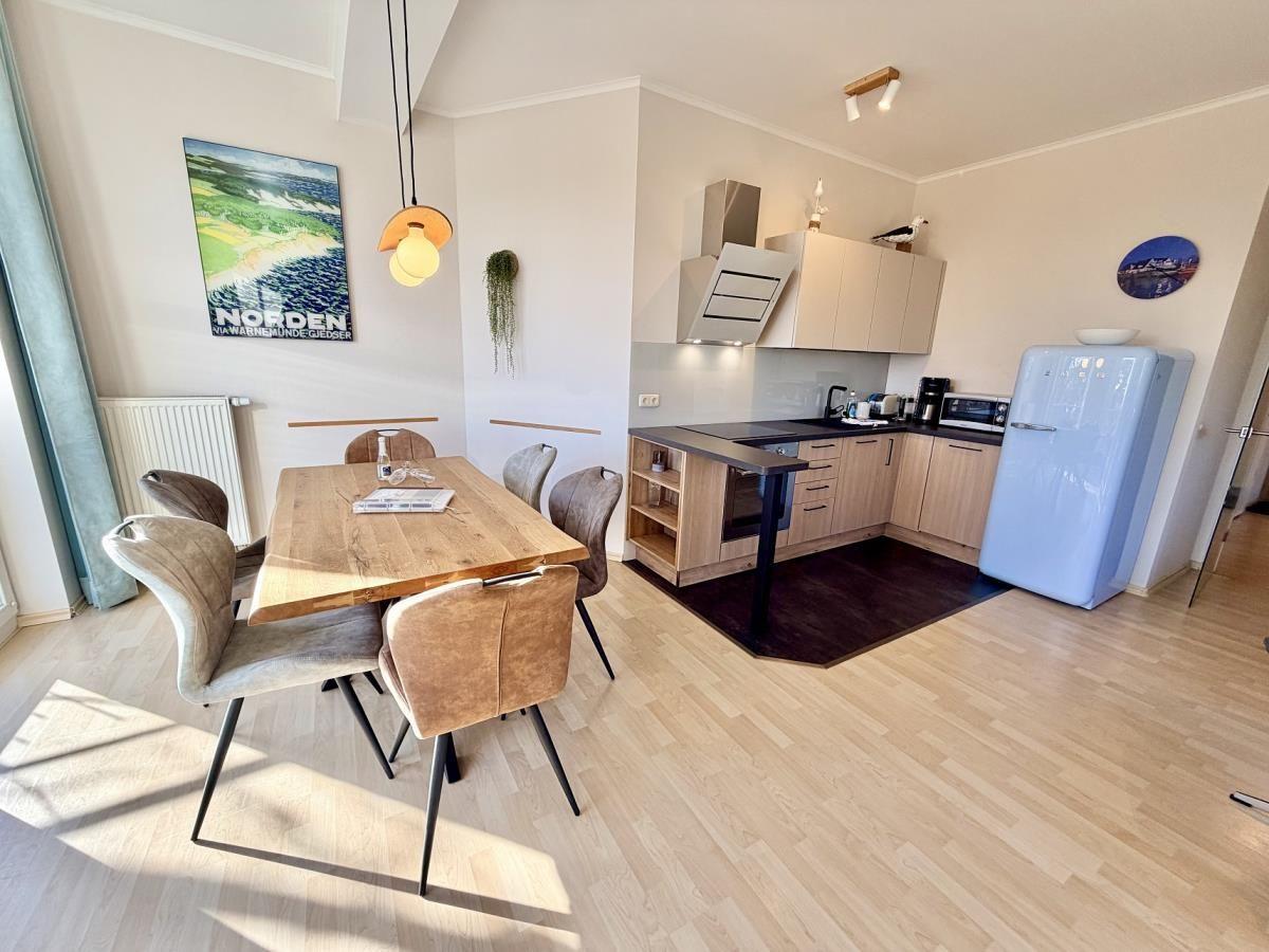 Essbereich mit Holztisch und Stühlen. Küche mit Kücheninsel und blauer Kühlschrank.
