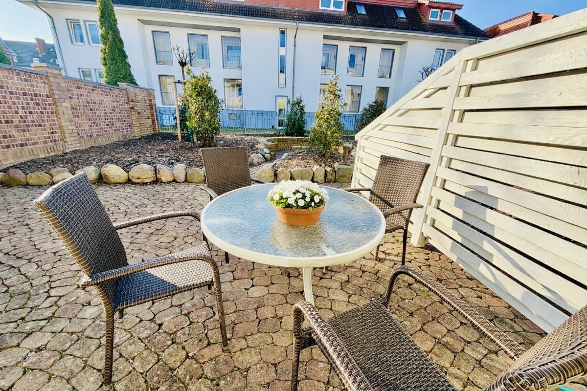 Garten mit runden Tisch und vier Stühlen, gepflastert mit Steinen und Pflanzen.