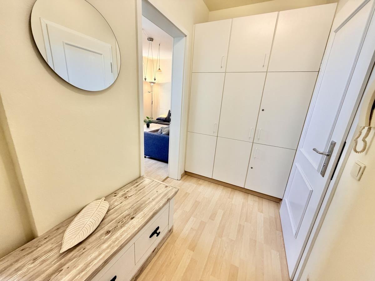Eingangsbereich mit Schuhschrank, Spiegel und Holzbank. Blick in Wohnzimmer mit Sofa.