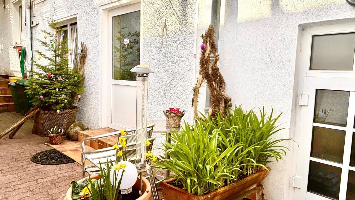 Hinterhof mit Pflanzen, Sitzgelegenheit und Heizgerät an weißer Wand