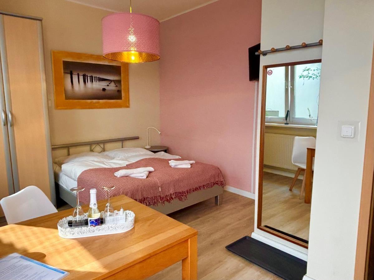 Schlafzimmer mit Bett, Tisch und Spiegel. Wandfarbe rosa. Deckenleuchte und Bild an der Wand.