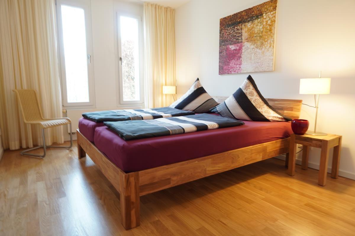 Schlafzimmer mit Holzbett, Fenstern und Wandbild.